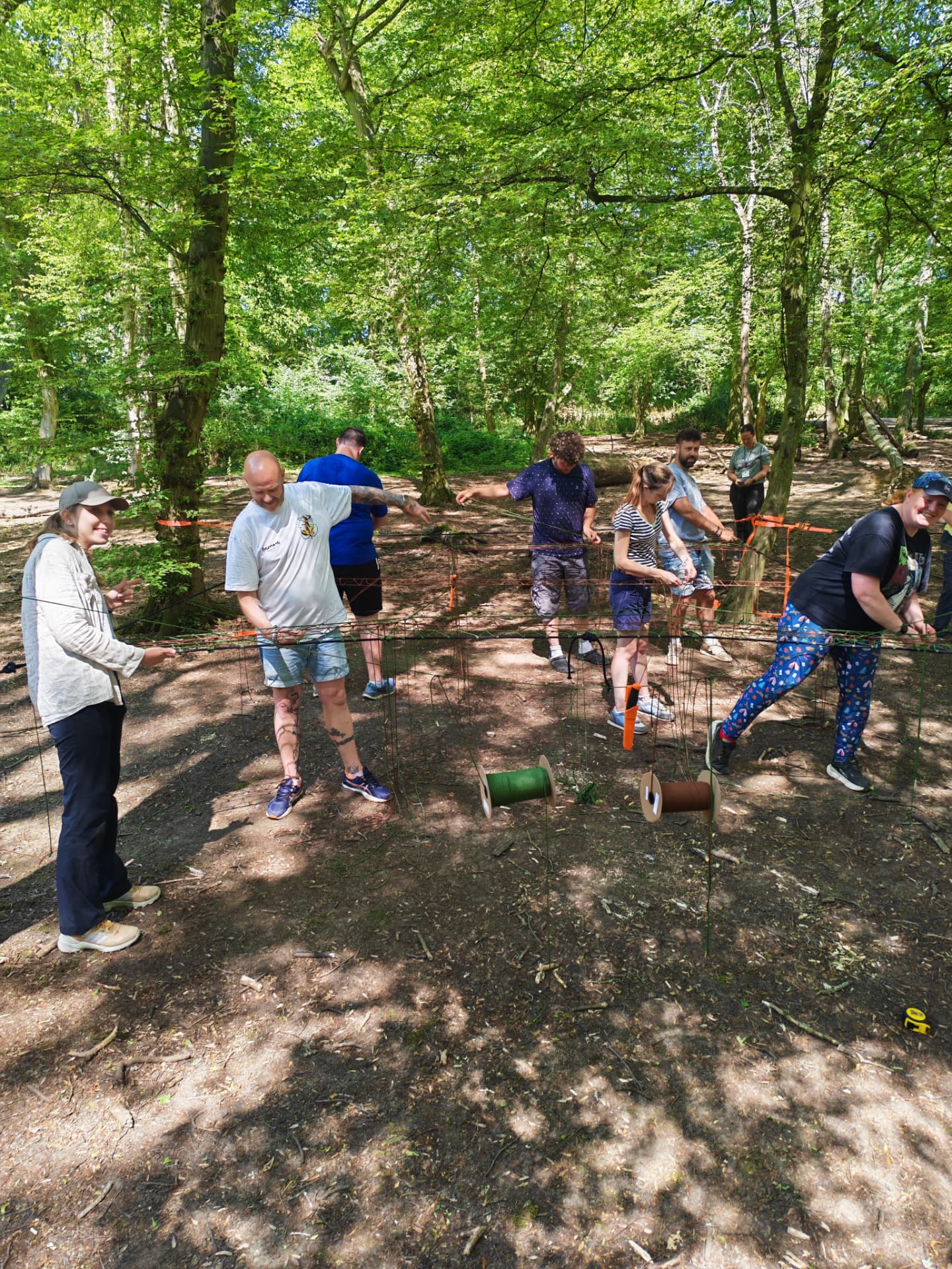 Participants weaving green and brown cord across net frames in the woods