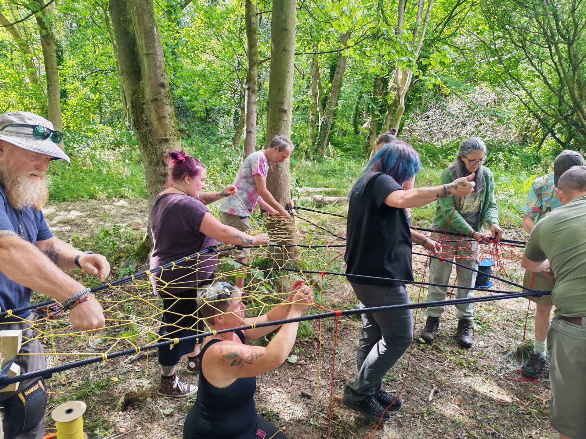 Course group weaving a large rope and cord TreeNet together in North Wales woodland